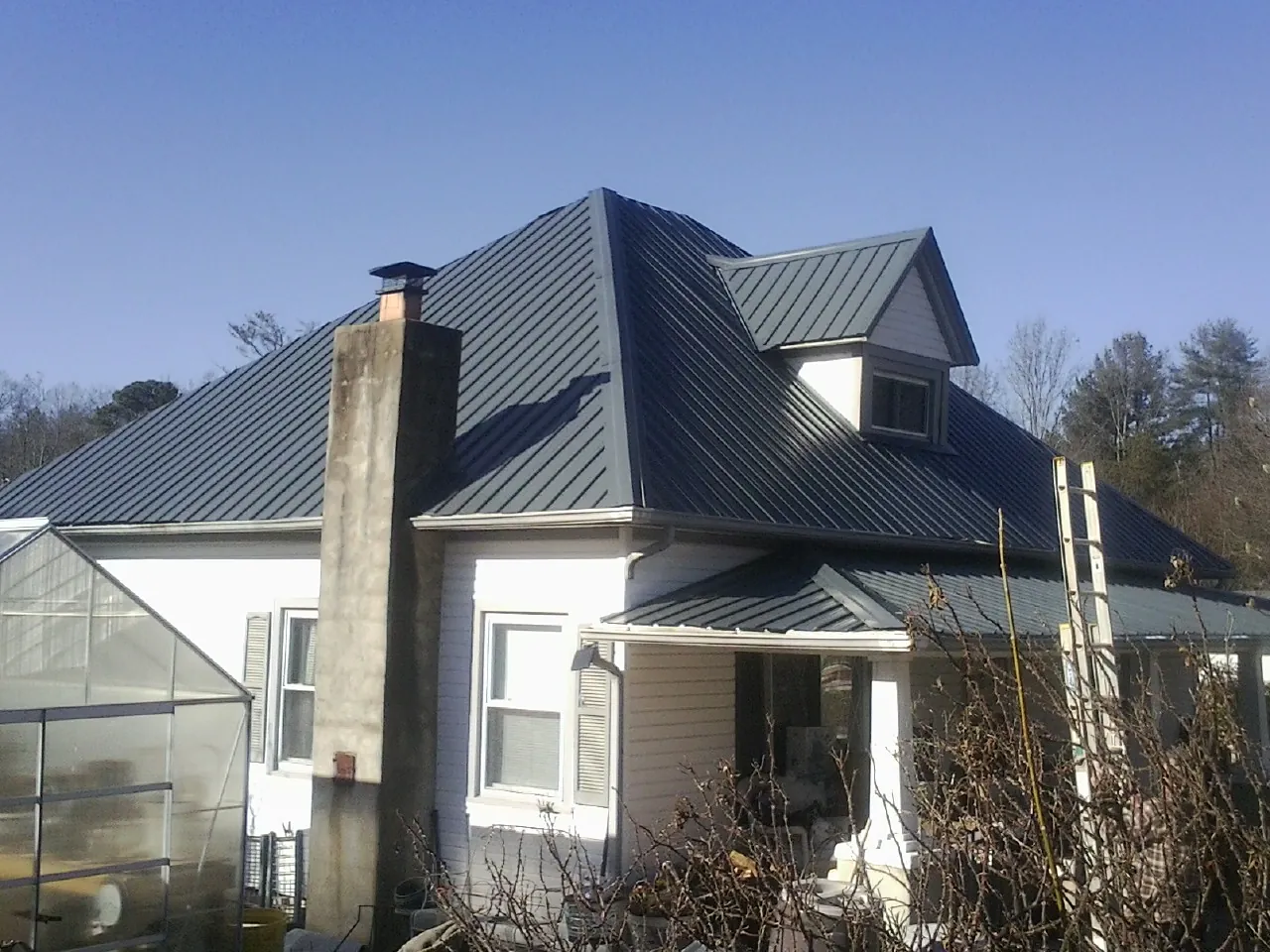 Dark blue standing seam metal roof on a white farmhouse with dormer — Slate & Tile Roof Repair by Roofing Brothers in Trent