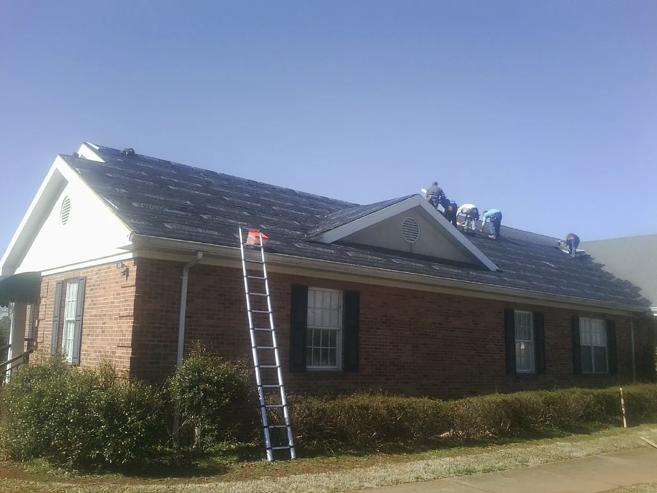 Crew tearing shingles off a brick ranch roof with a ladder set — Emergency Roof Repair work by our crew in Trent