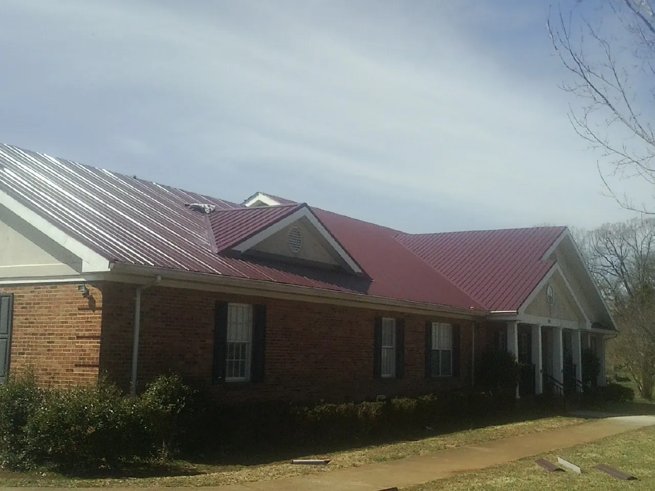 Red metal roof with gabled entries on a long brick building, from a Hail Damage Roof Repair job in Trent