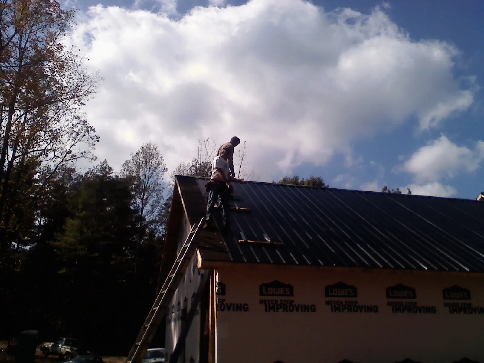 Roofer fastening dark metal panels high against a cloudy sky, from a Roof Inspection job in Trent