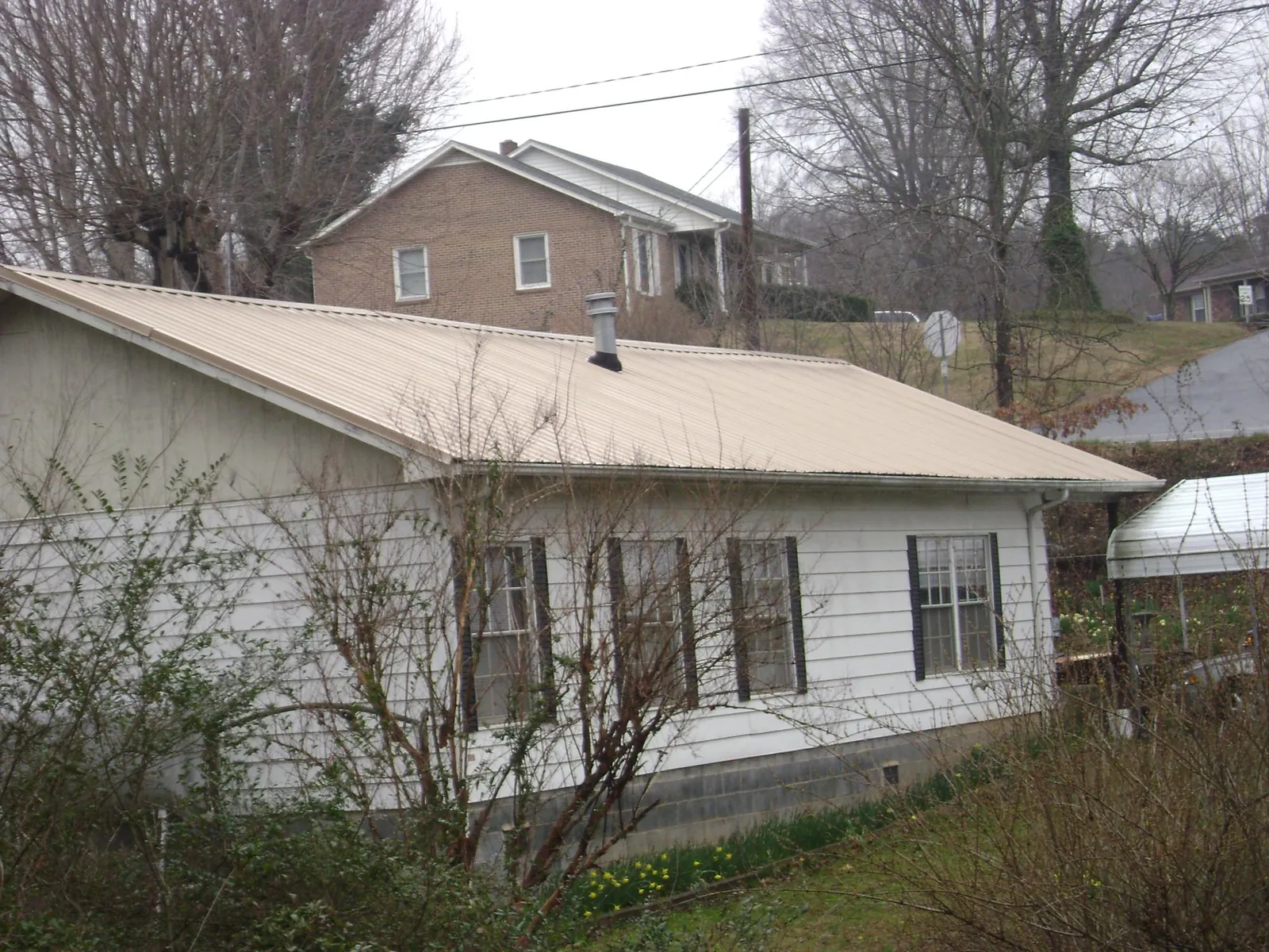 Tan metal roof on a white sided house set into a hillside — Commercial Roofing by Roofing Brothers in Trent