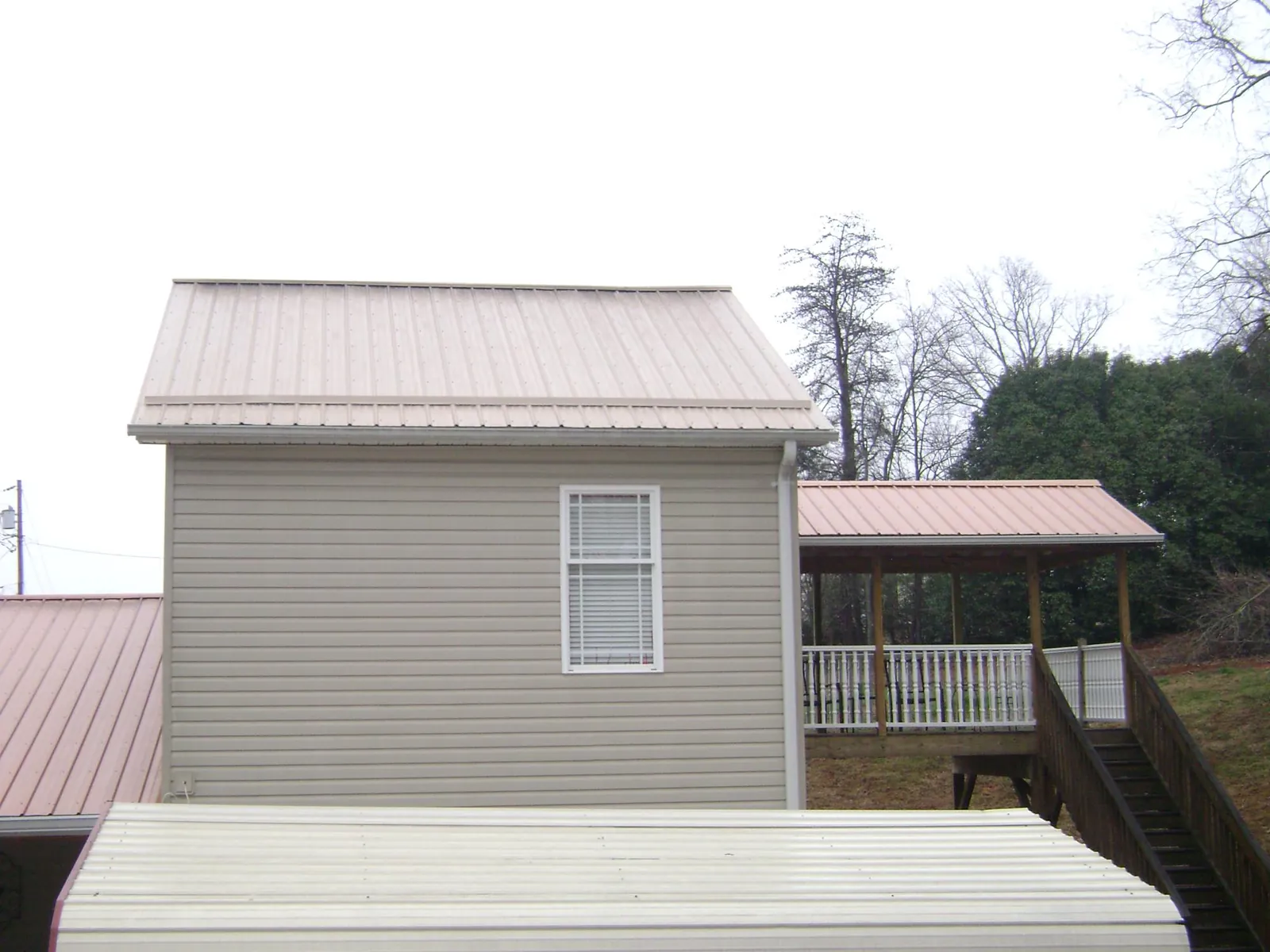 Tan metal roofs on a two story addition and attached porch, from a Roof Replacement job in Trent